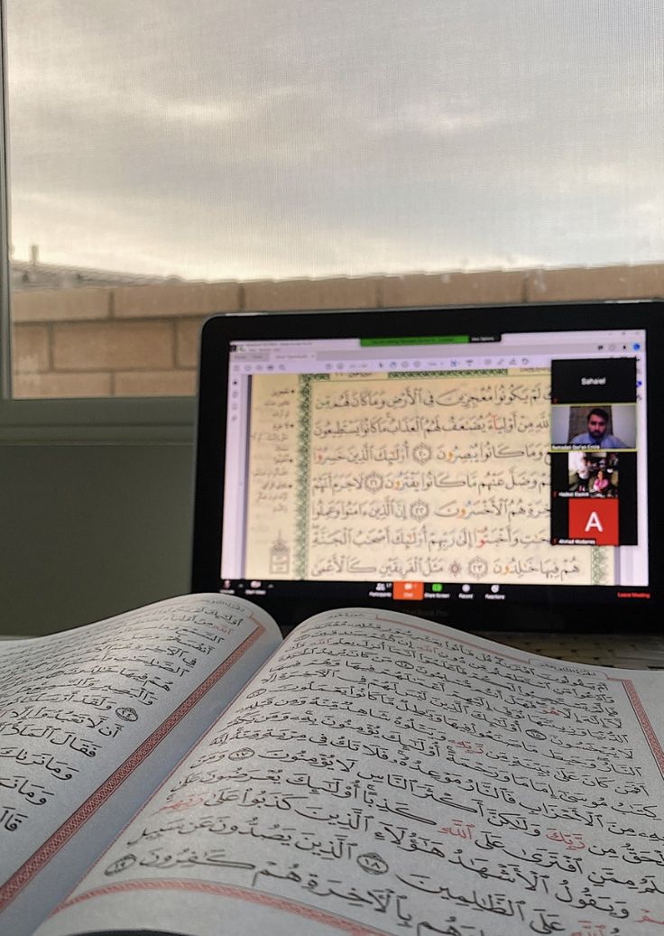 an open book sitting on top of a table next to a laptop computer and window