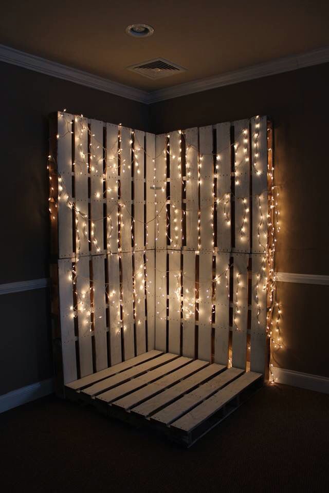 a bed made out of pallets with lights on the wall and behind it is a wooden slatted screen