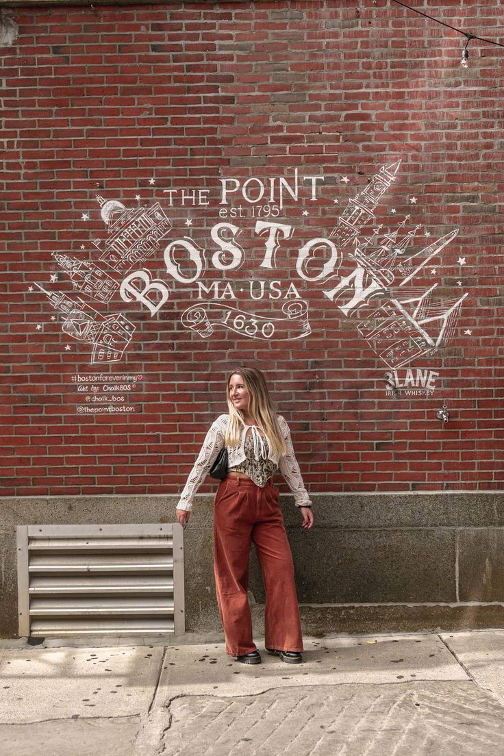 a woman standing in front of a brick wall with the word boston painted on it