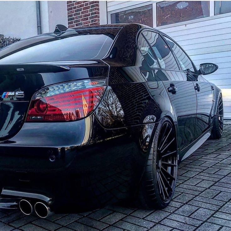 the back end of a black car parked in front of a house