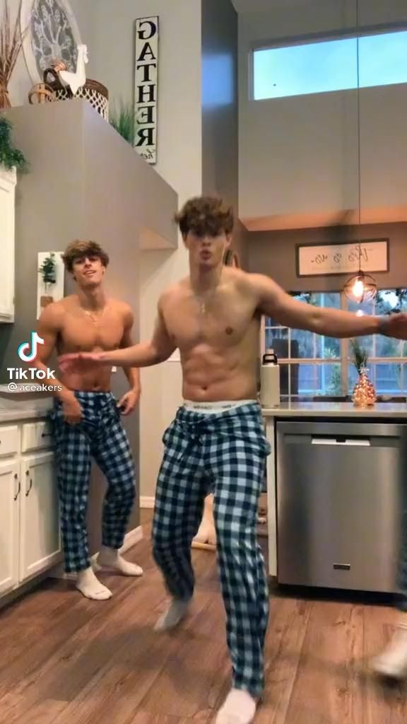 two young men dancing in the kitchen with their hands out and one man is wearing plaid pajama pants