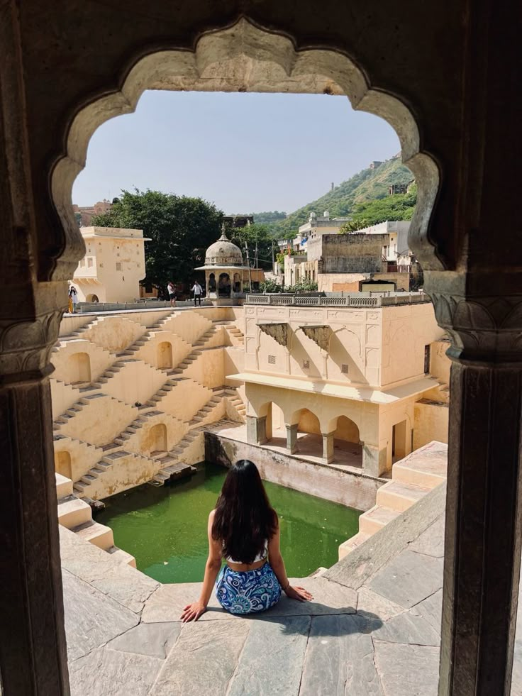 a woman sitting on top of a stone floor next to a pool of water in front of a building