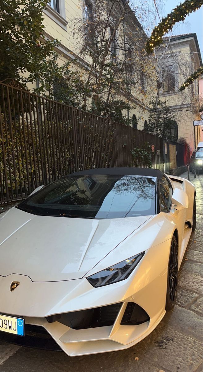 a white sports car is parked on the side of the street in front of a fence