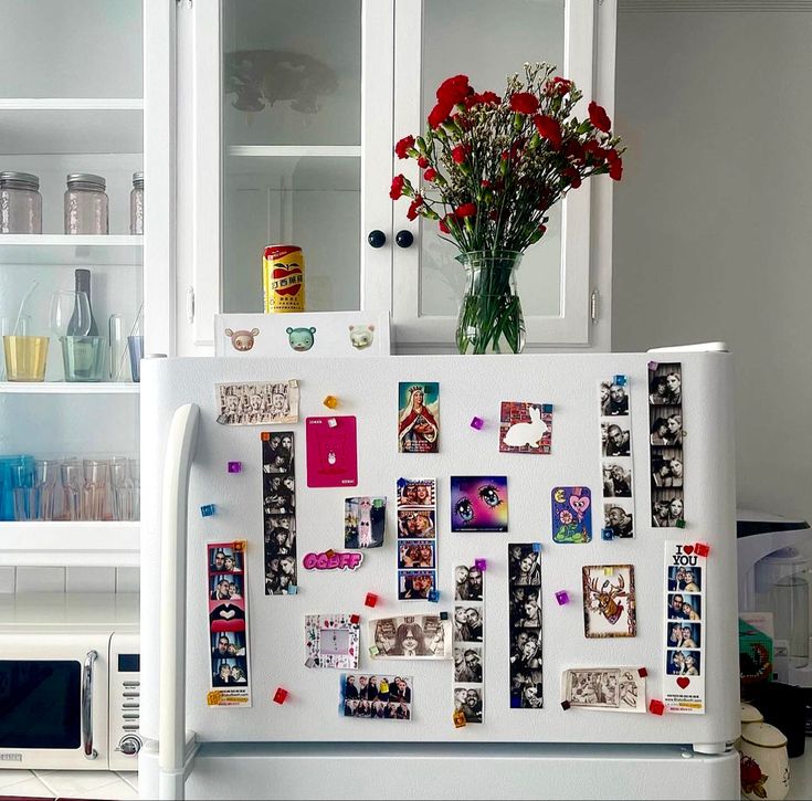 a refrigerator covered in magnets and pictures next to a vase with flowers on top