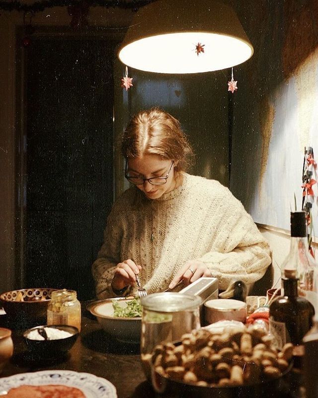 a woman sitting at a table with food in front of her and looking down on the plate