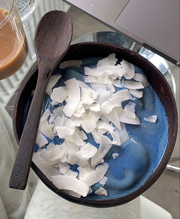 a bowl filled with coconut flakes next to a cup of coffee and a laptop