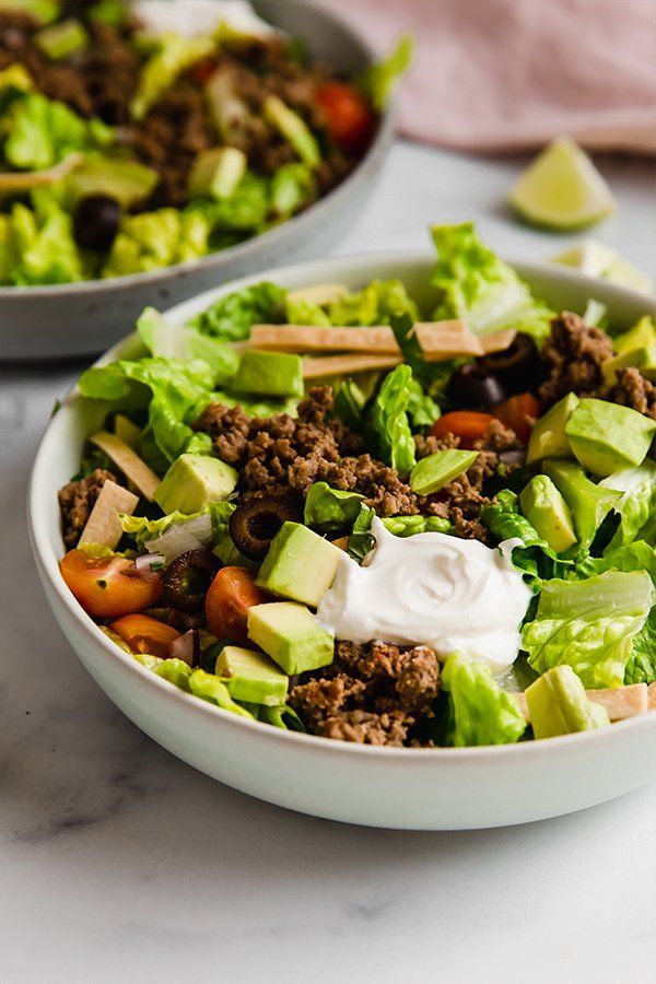 two bowls filled with lettuce, meat and vegetables