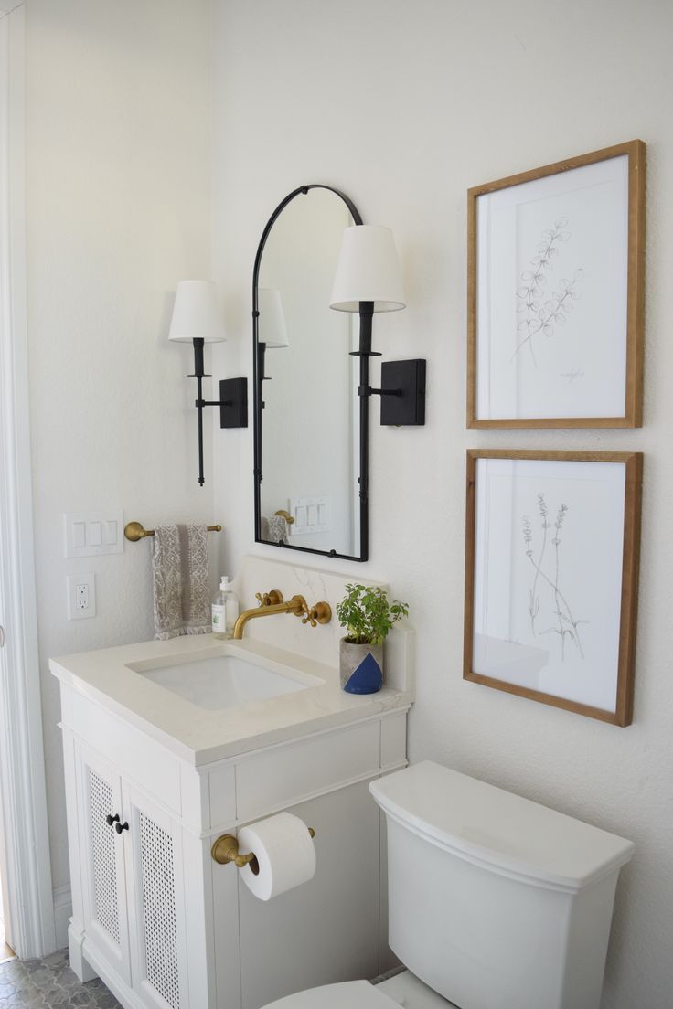 a white toilet sitting next to a sink in a bathroom under two framed pictures on the wall