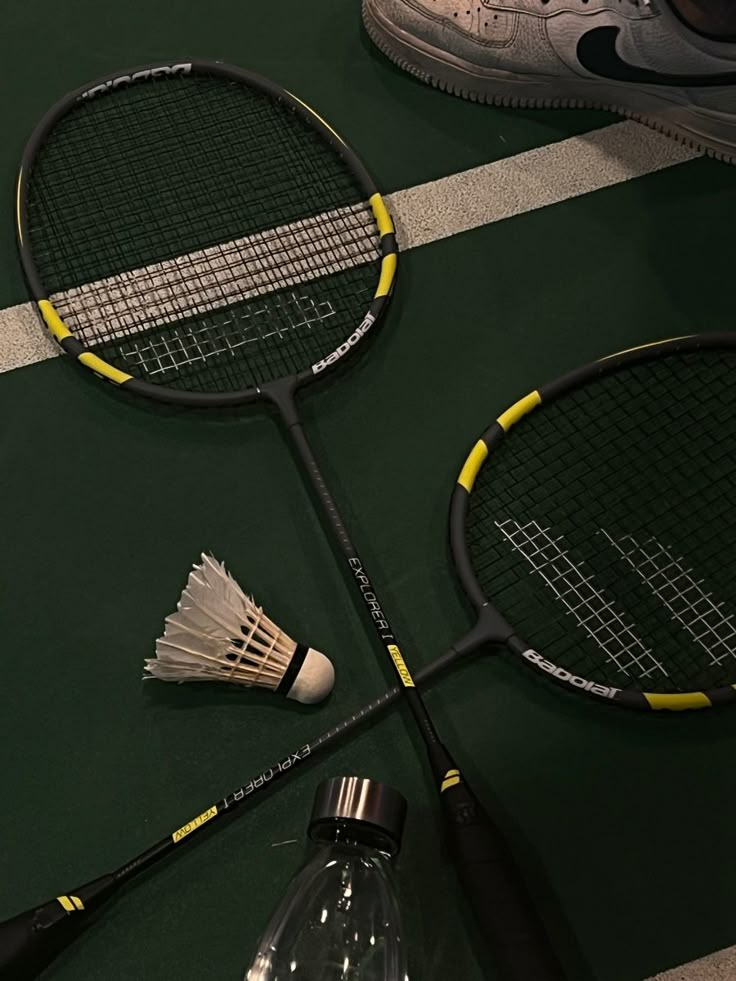 two tennis rackets are laying on the ground next to a bottle and badminton racquets