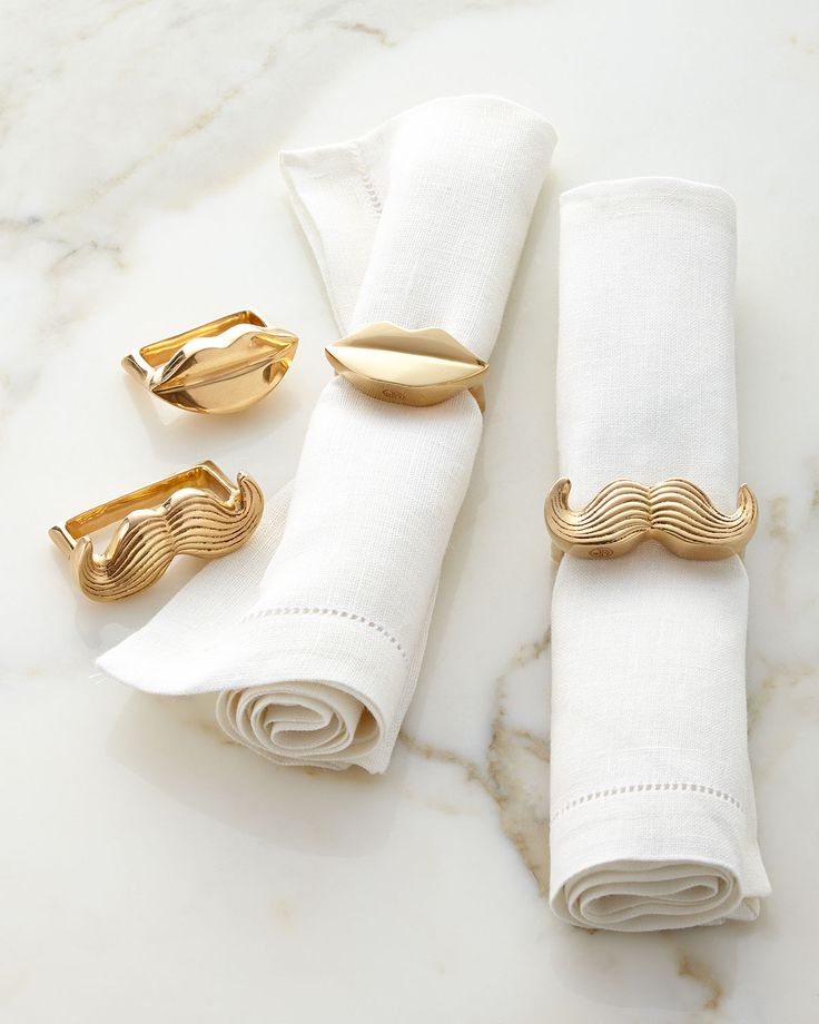 three napkin rings and two napkin holders on a marble countertop with white linens