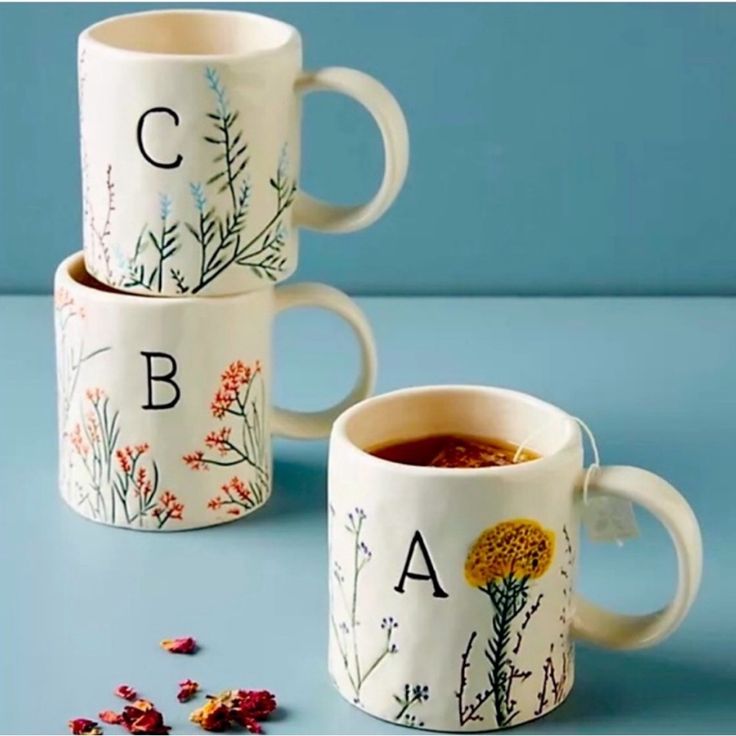 three coffee mugs with flowers and letters on them