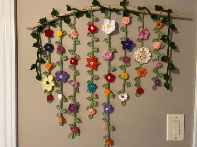 crocheted flowers hang from a branch on the wall next to a light switch