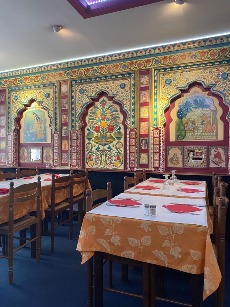 the interior of a restaurant with many tables and chairs in front of colorful paintings on the wall