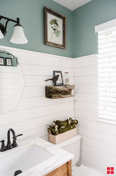 a white toilet sitting next to a bathroom sink under a light above a mirror on the wall