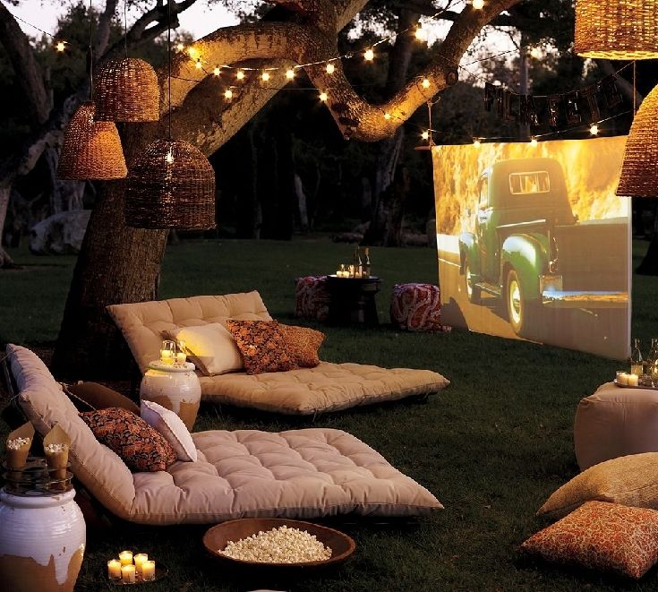 an outdoor movie is set up in the grass with lights strung over it and pillows on the ground