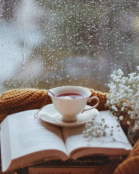 a cup of coffee sitting on top of an open book next to a window covered in raindrops