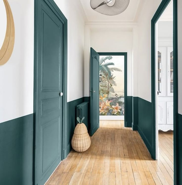 an empty hallway with green doors and wooden floors in front of a mirror on the wall