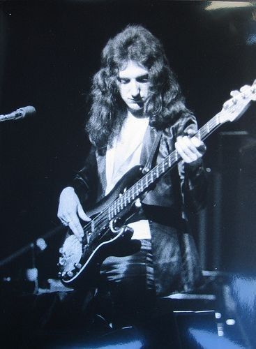 a black and white photo of a man with long hair playing an electric bass guitar