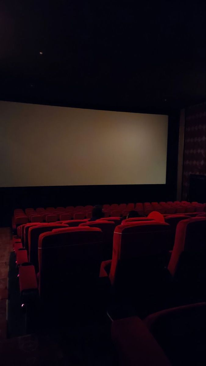 an empty theater with red seats and a projector screen in the middle of the room