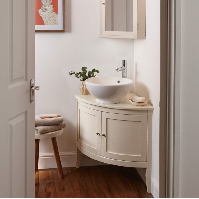 a white sink sitting under a bathroom mirror next to a wooden stool with a plant on it