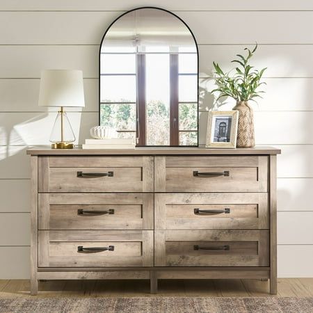 a dresser with a mirror on top of it next to a lamp and vase in front of a window