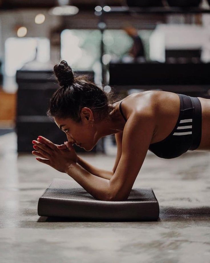 a woman doing push ups on a yoga mat in a gym setting with her hands together