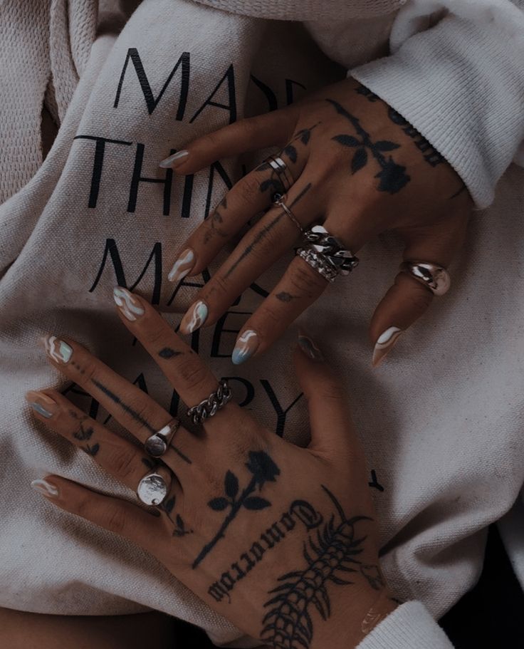 a woman's hands with tattoos and rings on her left hand, wearing a white sweatshirt