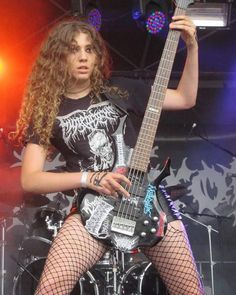 a woman in fishnet stockings and tights holding a guitar on stage with lights behind her