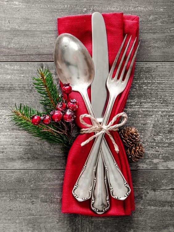 two forks and spoons wrapped in red cloth with pine cones on the side next to them