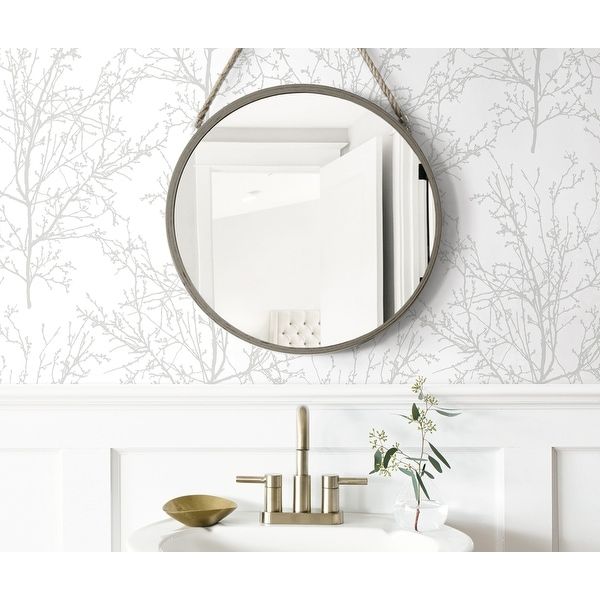 a bathroom sink under a round mirror next to a white wall with trees on it