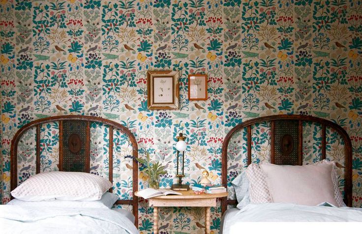 two twin beds in a room with floral wallpaper on the walls and side tables