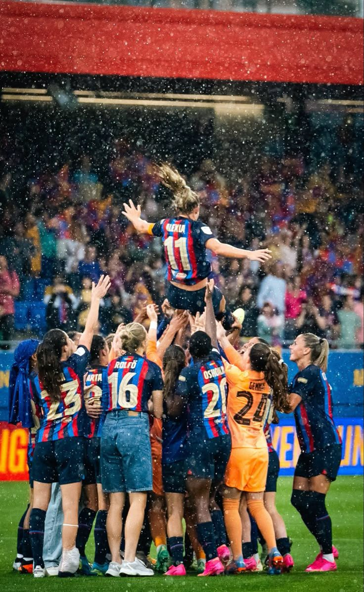 a group of women standing around each other on top of a soccer field in the rain