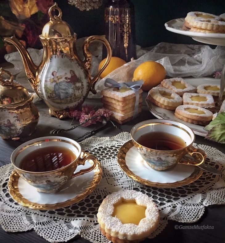 tea and pastries sit on a table with lace doily, flowers, and gold trimmings