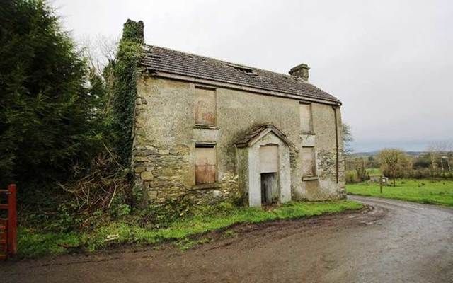 an old stone building sitting on the side of a road next to a lush green field