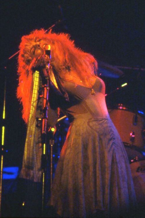 a woman with red hair standing in front of a microphone and singing into a mic