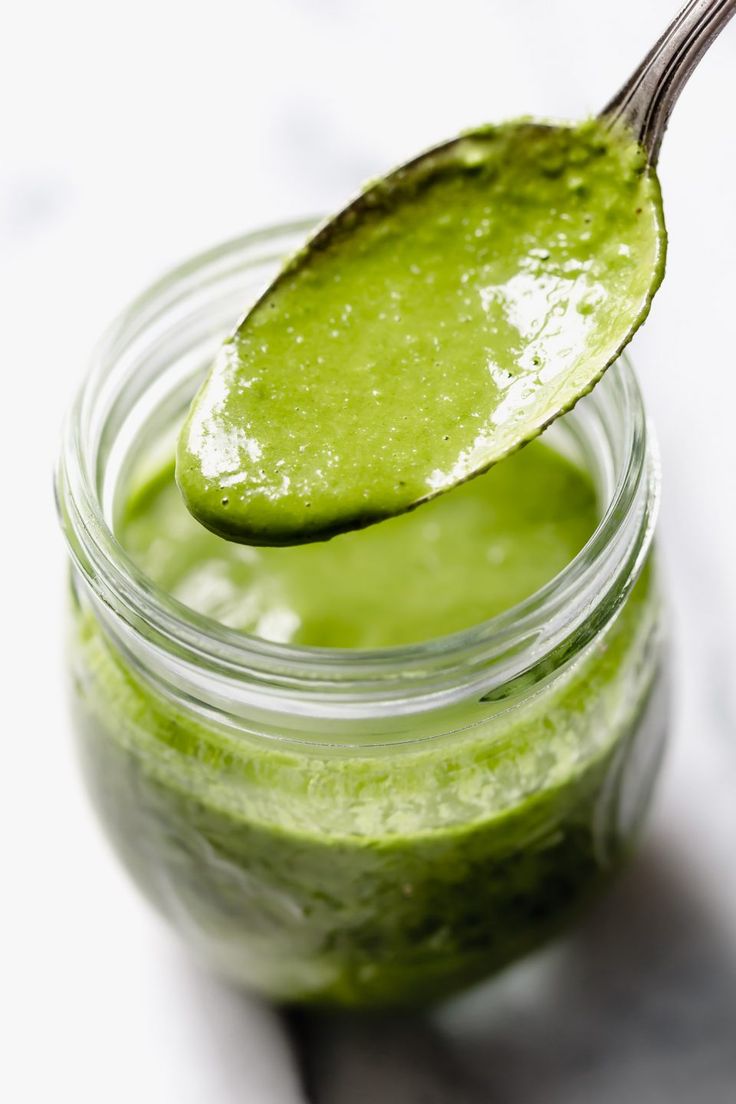 a spoon full of green liquid sitting on top of a jar