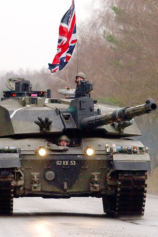 an army tank driving down the road with a british flag flying from it's roof