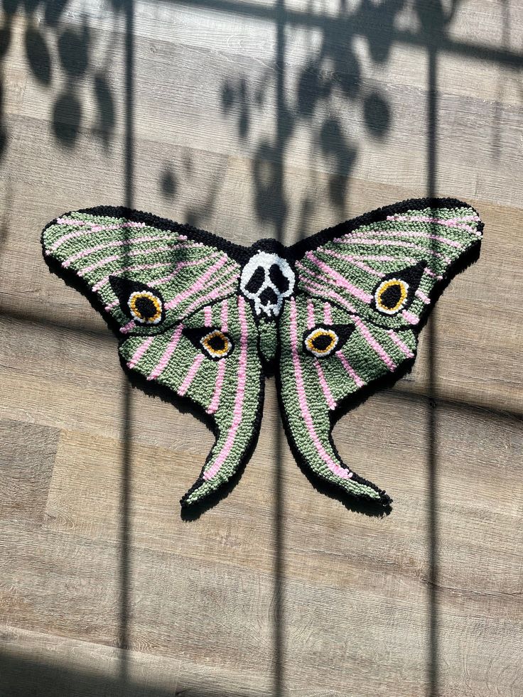 an embroidered butterfly sitting on top of a wooden floor next to a metal caged wall