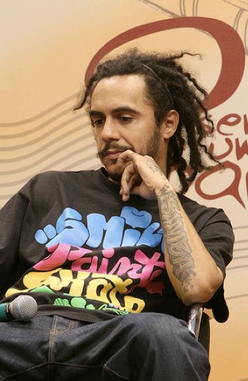 a man with dreadlocks sits in a chair and looks off to the side