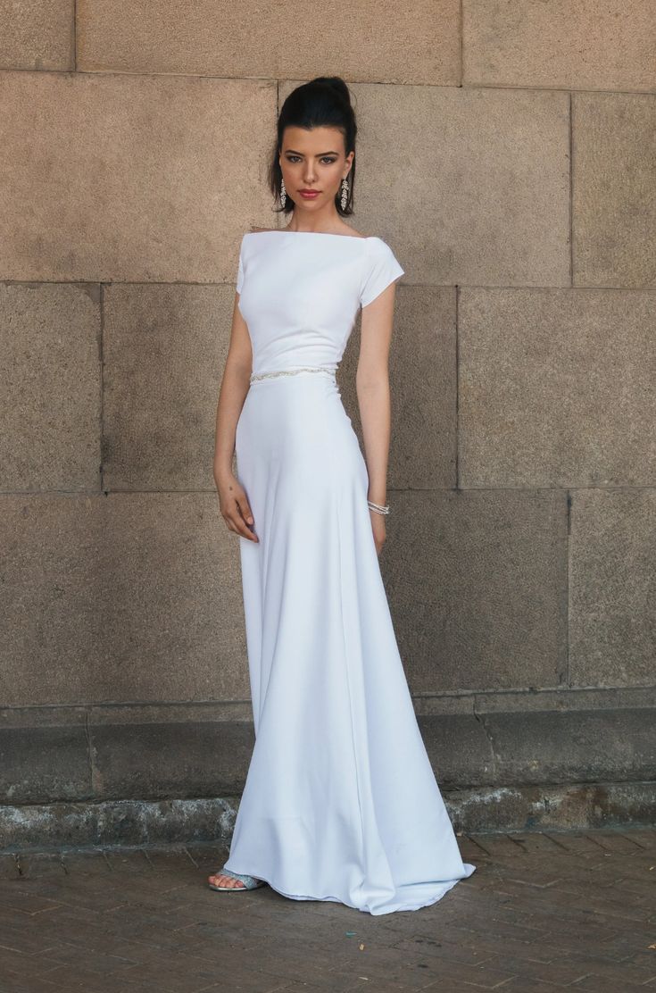 a woman standing in front of a wall wearing a white dress