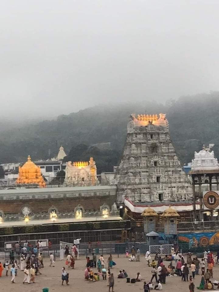 many people are walking around in front of a temple on a foggy day with mountains in the background