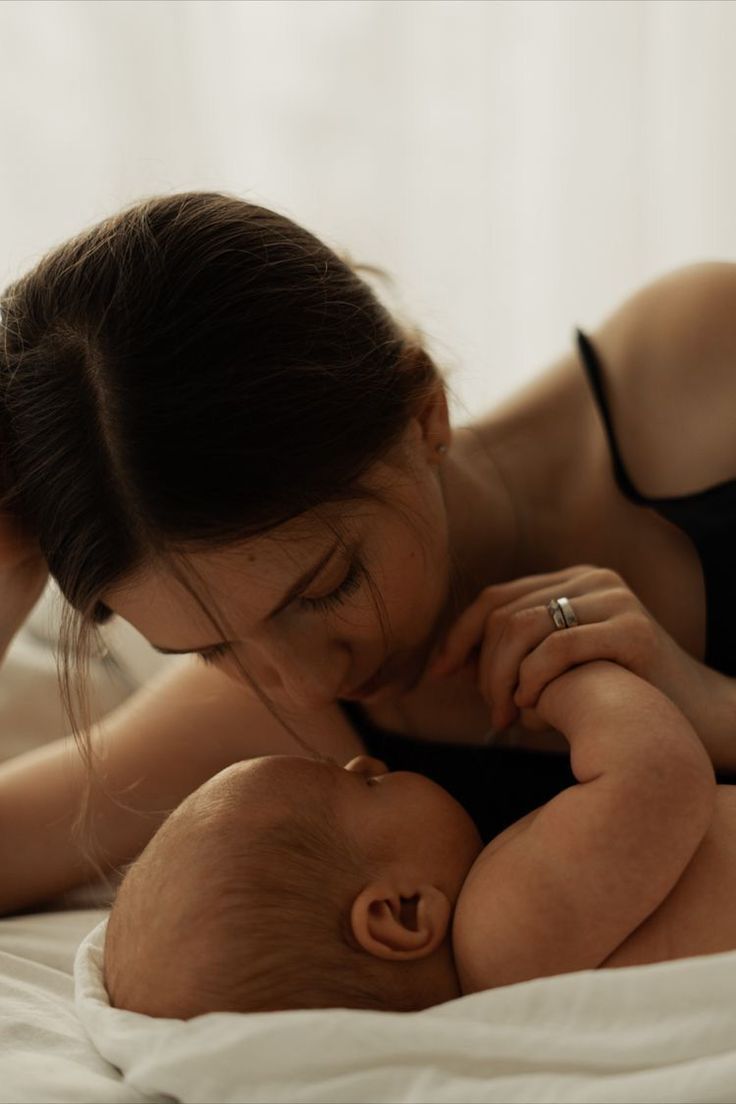 a woman is kissing her baby while laying on it's back in the bed