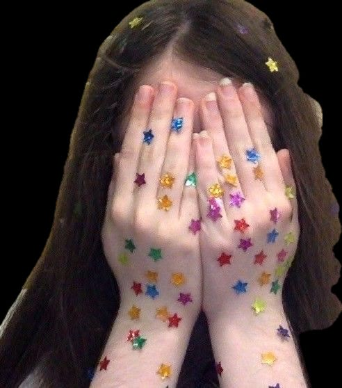 a girl with her hands on her face covered by colorful stars painted on her body