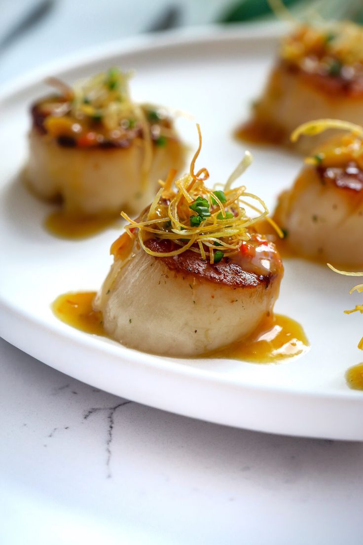 some scallops are sitting on a white plate with sauce and garnish