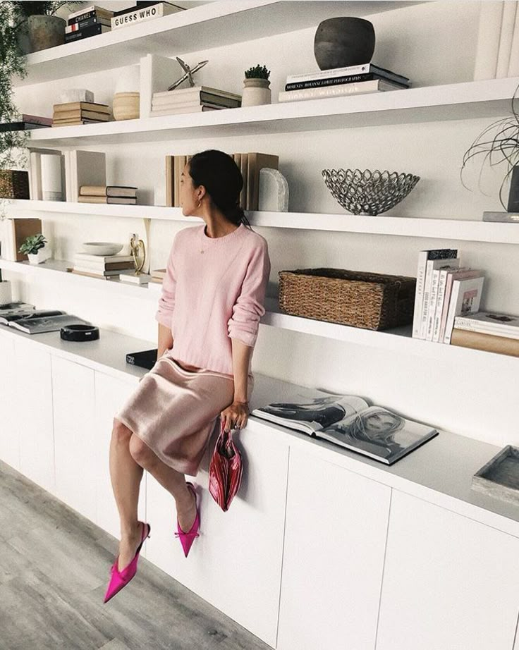 a woman sitting on the ledge of a bookshelf