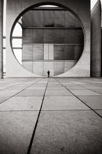 a black and white photo of a person standing in front of a large circular building