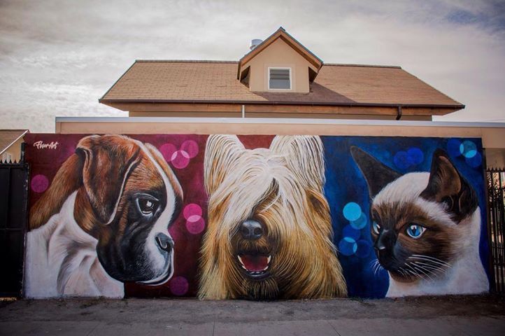 two dogs and one cat painted on the side of a building with a fence in front of it