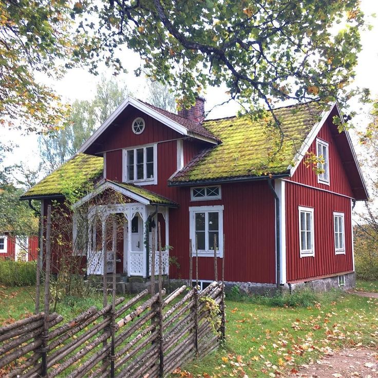 a red house with a green roof next to a wooden fence and some leaves on the ground