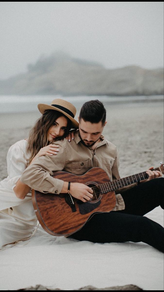 a man and woman sitting next to each other on the beach with a guitar in their hands