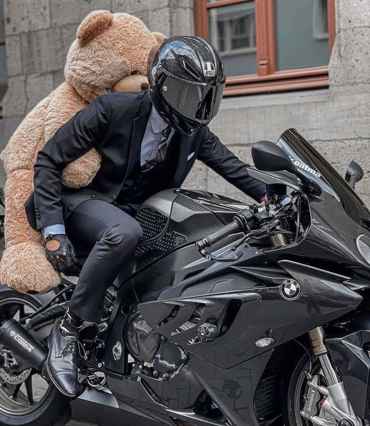 a man in a suit and helmet sitting on a motorcycle with a large teddy bear